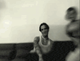 a man is sitting on a couch with a woman standing behind him in a black and white photo .