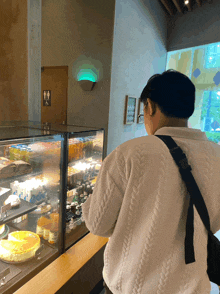 a man in a white sweater looks at a display case of food