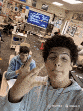 a young man taking a selfie in a classroom with a sign on the wall that says ' british army '