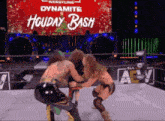 two wrestlers are wrestling in front of a sign that says holiday bash