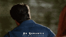 a man in a blue shirt stands in front of a sign that says mr romantic the boy creation