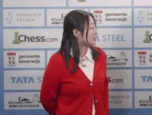 a woman in a red jacket is standing in front of a wall that says chess.com and tata steel