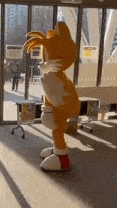 a mascot dressed as tails from the video game sonic the hedgehog is standing in front of a glass door .