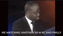 a man in a suit and tie is watching another sb w kc and philly on tv .