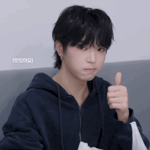 a young man in a blue hoodie gives a thumbs up in korean