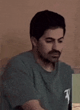 a man with a beard is sitting at a table looking at a laptop .