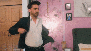 a man in a suit and white shirt is standing in a bedroom with his jacket open .
