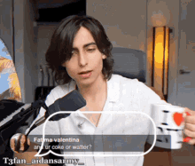 a man in a white shirt is sitting in front of a microphone and holding a cup with a heart on it