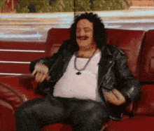 a man with a mustache and a leather jacket is sitting on a couch .