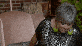 a woman with gray hair is sitting on a couch wearing green earrings .