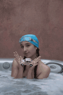 a girl in a hot tub holds a pink hello kitty car and a toothbrush