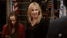 a woman is making a funny face in front of a wall of plaques with the nbc logo in the corner