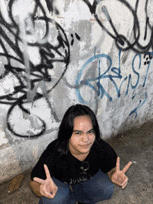 a girl giving a peace sign in front of a wall with graffiti that says rust