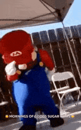 a person dressed as mario is standing in front of a fence and chairs .