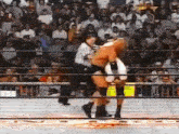 two wrestlers are fighting in a wrestling ring with a referee .