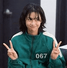 a woman in a green jacket is making a peace sign .