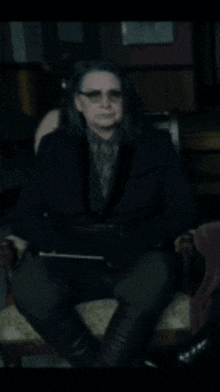 a woman with glasses is sitting in a chair in a dark room