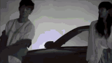 a man and a woman are standing next to each other in front of a car