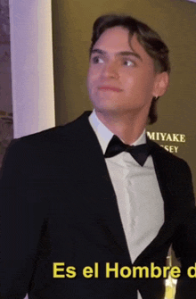 a man in a tuxedo and bow tie is standing in front of a sign that says miyake