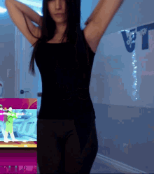 a woman in a black tank top is dancing in front of a white board with a blue flag on it