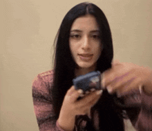 a woman with long black hair is holding a cell phone in her hand