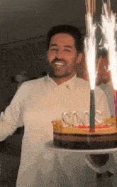 a man in a white shirt is holding a birthday cake with candles in the shape of numbers .