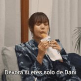 a woman sitting on a couch eating a sandwich with the words devora si eres solo de dani written below her