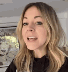 a woman with blonde hair and a black shirt is making a funny face .