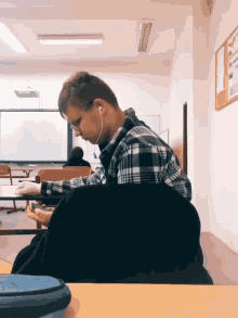 a man in a plaid shirt is sitting at a desk in a classroom