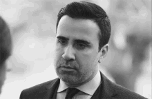 a man with a beard is wearing a suit and tie and looking at the camera .