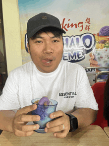 a man wearing an essential fear of god t-shirt is holding a cup of ice cream