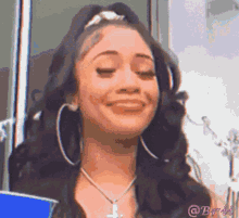 a woman wearing hoop earrings and a necklace smiles