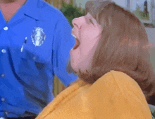 a woman in a yellow sweater is yawning in front of a police officer in a blue shirt