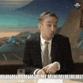 a man in a suit and tie is sitting at a table with the words mimi mimi mimi mimi mimi mimi written on the table