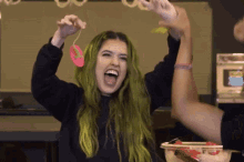 a woman with green hair is laughing while holding a candy