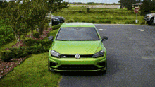 a green volkswagen golf r is parked in a parking lot next to a grassy field .