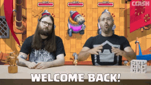 two men are sitting at a table with the words welcome back