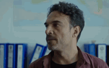 a man with curly hair is standing in front of a row of blue folders .
