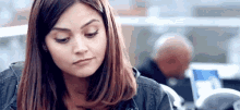 a woman is sitting at a table with a laptop in front of her and looking down .