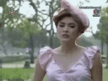 a woman in a pink dress and hat stands in a park