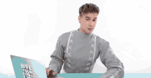 a young man wearing a grey sweater says " what "