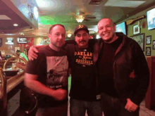 three men posing for a picture one of whom is wearing a shirt that says oakland