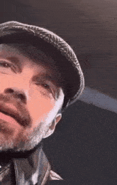 a man with a beard and hat is looking at the camera .