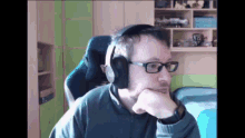 a man wearing headphones and glasses sits in a chair with his hand on his chin