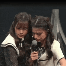 a girl holding a microphone while another girl looks on