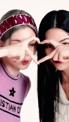 two women are making a heart shape with their hands and one has a christian dior sweater on