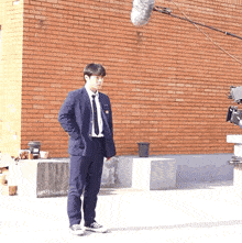 a man in a suit stands in front of a brick wall