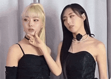 two women are standing next to each other and one of them is touching her face .