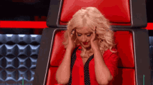 a woman in a red shirt is sitting in a red chair covering her ears