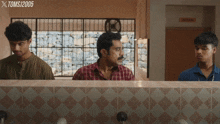 three men are looking at their faces in a bathroom with a sign that says indian